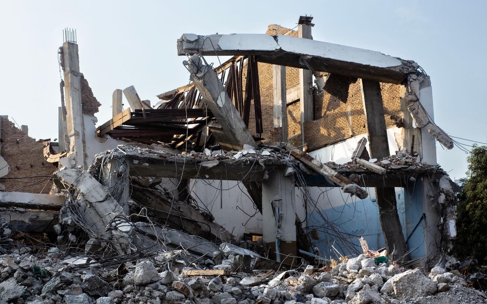 A partially demolished building surrounded by piles of broken concrete and construction rubble.