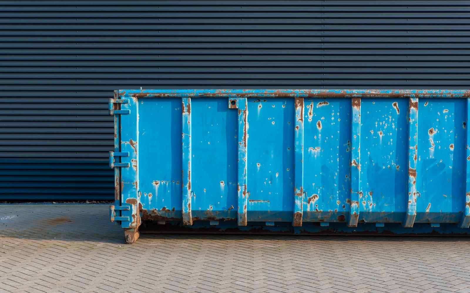 A blue roll-off dumpster container parked on hardstanding, ready for loading.